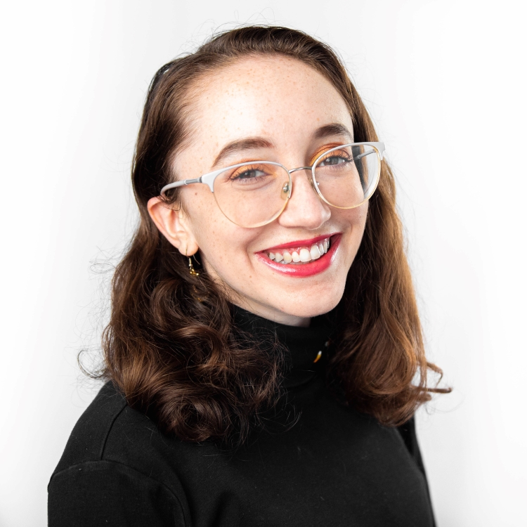 Rosalind Helsinger, Outstanding Senior Scholar-Fall 2021-Student has medium length brown wavy hair. She is wearing a black turtleneck shirt and glasses. She is smiling and wearing red lipstick.