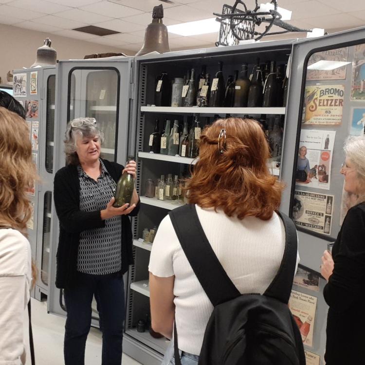 "Bureau of Archeological Research Collections Field Trip with Dr. Geoffrey Thomas. Pictured is Dr. Paulette McFadden with the BAR, talking about bottle shape and manufacturing over time."