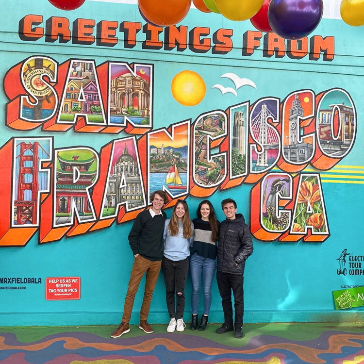 "Travis Zittrauer, Jamie Guterman, Trystan Loustau, and Gustavo Capone in Front of San Francisco colorful sign."