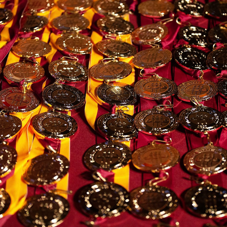 "Honors Medallions on Garnet Tablecloth, with both bi-color garnet and gold ribbons and solid garnet ribbons. Medallions and ribbons are displayed vertically next to one another."