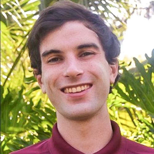 Image of Honors in the Major Student, Jackson Alley. Student has brown longer short hair and is smiling. He is wearing a garnet shirt with collar, standing in front of outdoor plant.