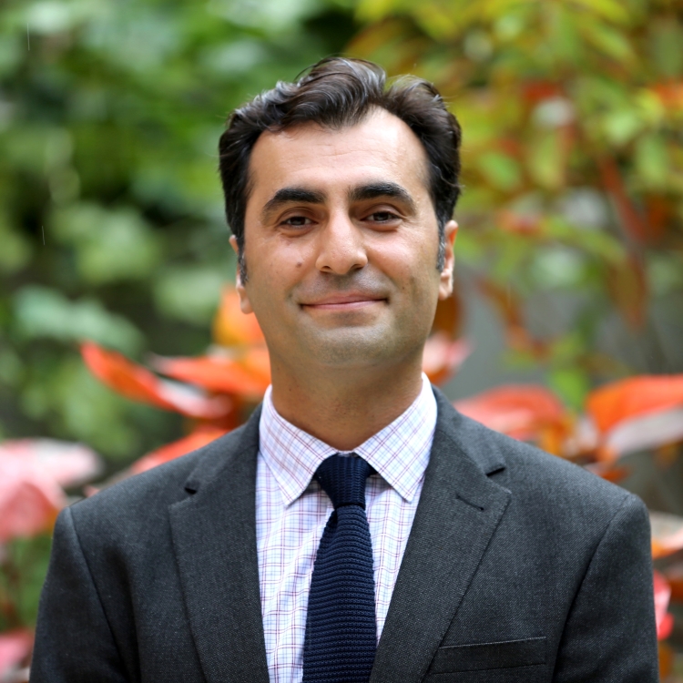 Dr. Azat Gundogan is wearing a dark gray blazer with white buttoned down shirt with light pastel plaid design. Dark tie.