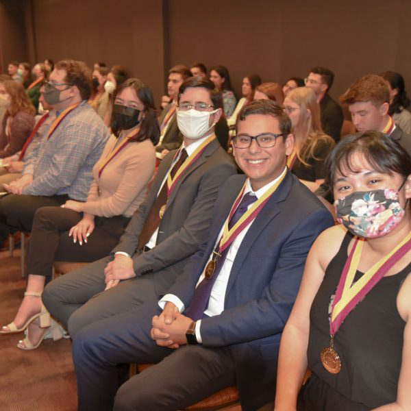 [FSU News Photo] Fall 2021 Honors Medallion Ceremony. Students in business casual wear are sitting in chairs, wearing their Honors Medallions and smiling at the camera. Camera angle was from the students' left hand side.