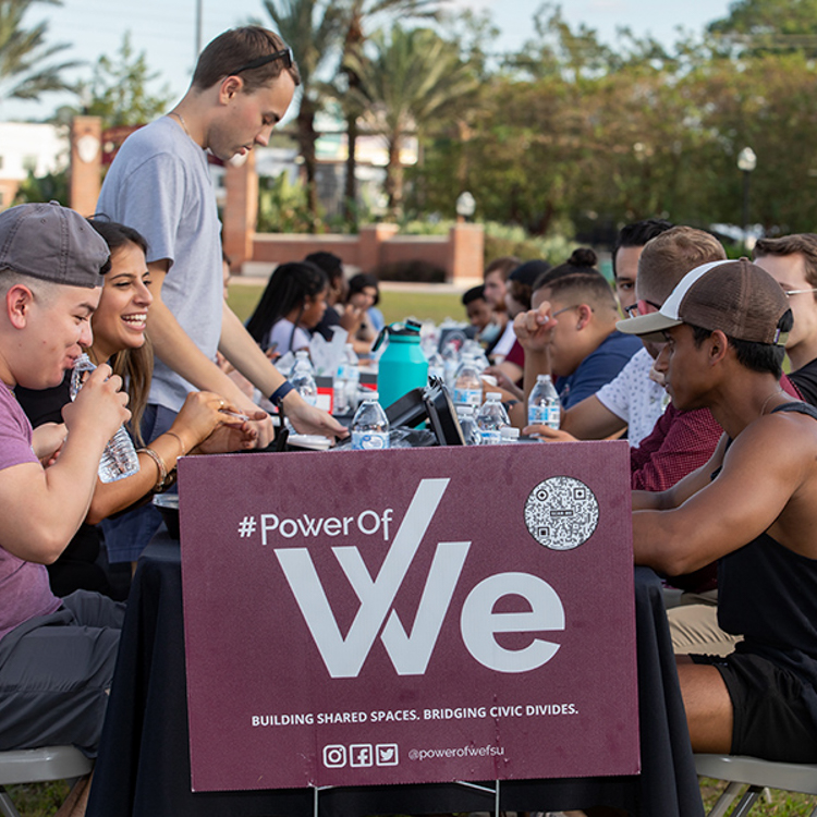 Power of WE's The Longest Table at FSU Event. Students sitting at long banquet table sharing a meal and discussion. Also link to FSU News article.