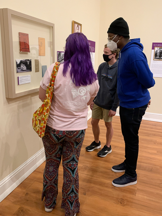 Museum Exhibit Tour-Florida Women's Activism. Three students looking at glassed and framed artifacts on hang on the wall in the Museum of Florida History.