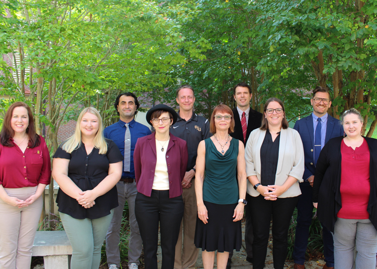FSU Honors Program Staff & Faculty Group Photo. Staff & Faculty are standing in front of crepe myrtle trees on the eastside of the HSF Building.