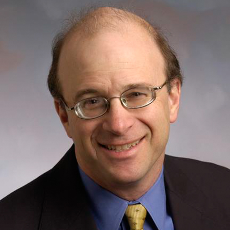 Dr. G. Kurt Piehler, Ph.D.-Dr. Piehler is wearing a dark suit jacket, blue button down dress shirt and gold tie. He is also wearing glasses and smiling. 