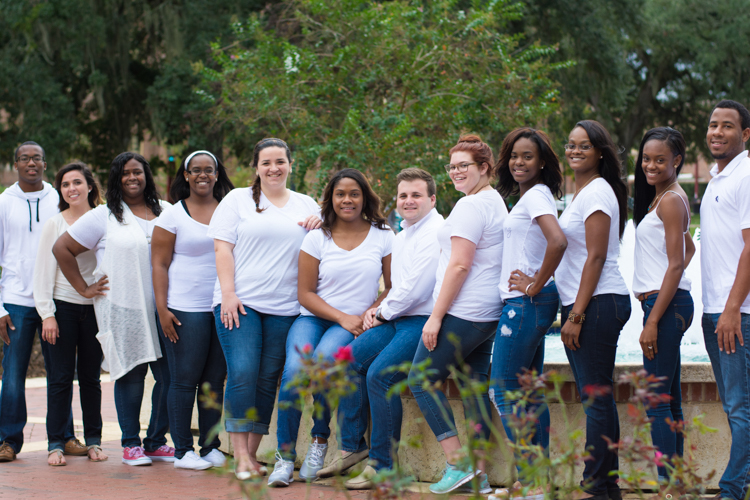 Unconquered Scholars group photo. Students are all wearing blue jeans and white shirts. The students are outside with trees in the background. Link also to Unconquered Scholars webpage.