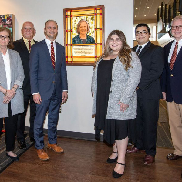 Unveiling of Former Dean of Undergraduate Studies, Karen Laughlin, memorial stained glass picture. Pictured from left to right are are Sally McRorie (Provost), current Dean of Undergraduate Studies, Joe O'Shea, Cara Axelrod (FSU Admissions Counselor), Brendan Gonzalez (senior Unconquered Scholars student and recipient of inaugural Karen Laughlin Scholarship), and Jim Lee (Chair of Division of Undergraduate Studies Development Council). They are all standing on either side of the newly created stained glass memorial picture of Dean Karen Laughlin, which includes her likeness in stained glass.