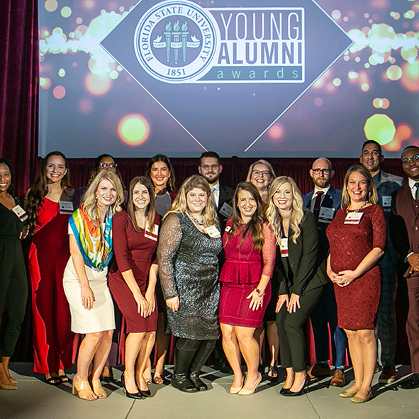 Group Photo at Young Alumni Awards on November 5, 2021. Everyone is in business attire/semi formal attire and smiling. Two former Honor Program students in the photo are Jesse Marks, back row center, and Jordan Rogers, front row far right.